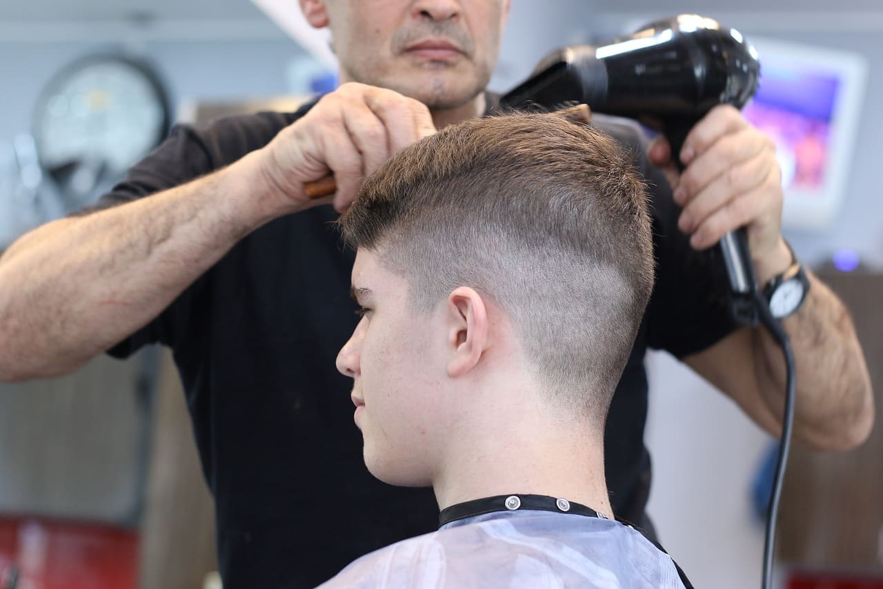 Peluquero secando el pelo a chico joven